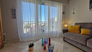 Ein Wohnzimmer mit einer Couch, einem Couchtisch mit dekorativen Vasen, transparenten Vorhängen und Blick auf Gebäude.