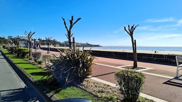 A coastal promenade with a paved walkway, greenery, and a view of the sea.