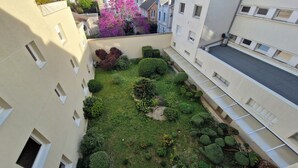Ein Innenhof mit vielfältigem Grün, darunter Sträucher und ein Baum mit rosa Blüten.