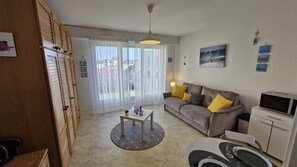 A living room with a sofa, coffee table, and a television. There is a sliding door leading to a balcony.