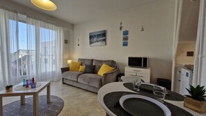 Ein modernes Wohnzimmer mit einer Couch, einem Esstisch, einem Fernseher und einem Kühlschrank.