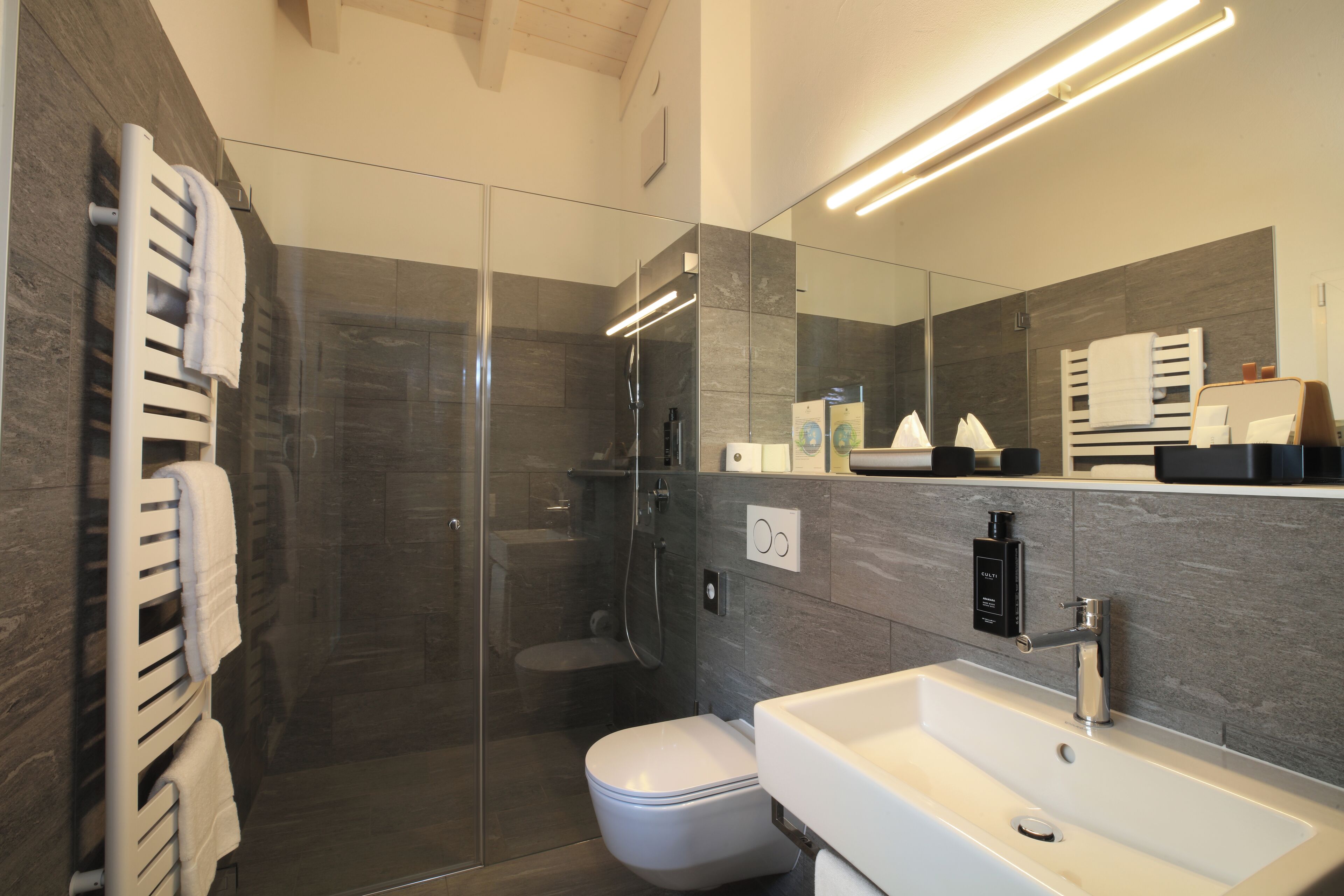 Un baño moderno con ducha de vidrio, lavamanos blanco y un espejo grande.