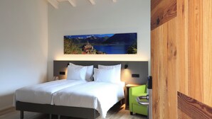 A modern bedroom with a large bed, a nightstand, a green chair, and a wall-mounted painting of a scenic landscape. - Charme Hotel al Torchio  (Ascona)