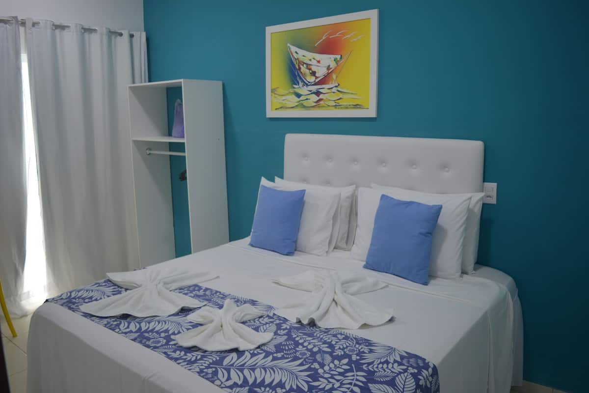 A hotel room with a bed, blue and white bedding, a white headboard, and a painting on the wall.