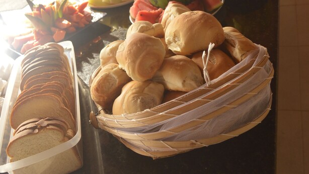 A buffet table with various food items including bread, pastries, and fruits. - Pousada Vovó Zilda (Maragogi)