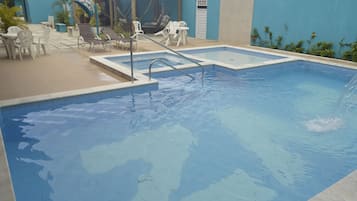 Una piscina con trampolín y sillas de descanso.