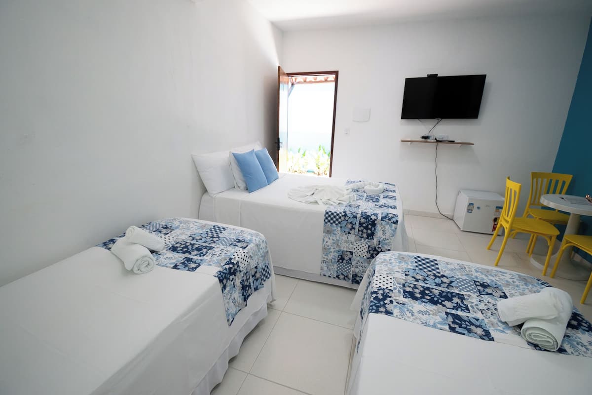 A hotel room with two single beds, a TV mounted on the wall, a small table with chairs, and a window with a view.