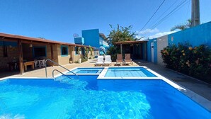 A swimming pool area with two pools, lounge chairs, and a building with a blue facade. - Pousada Vovó Zilda (Maragogi)