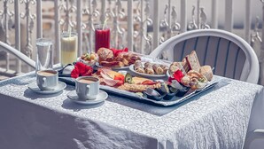 A table set with breakfast items, including pastries, bread, and a drink, on a balcony with a view of the sea.
