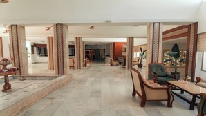 A spacious lobby with marble flooring, patterned columns, and a reception desk.