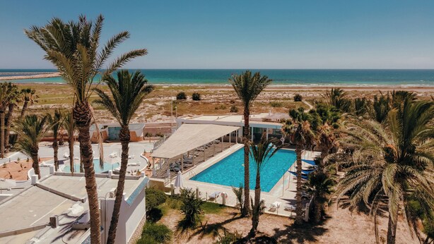 A resort with a swimming pool, palm trees, and a view of the beach and ocean.