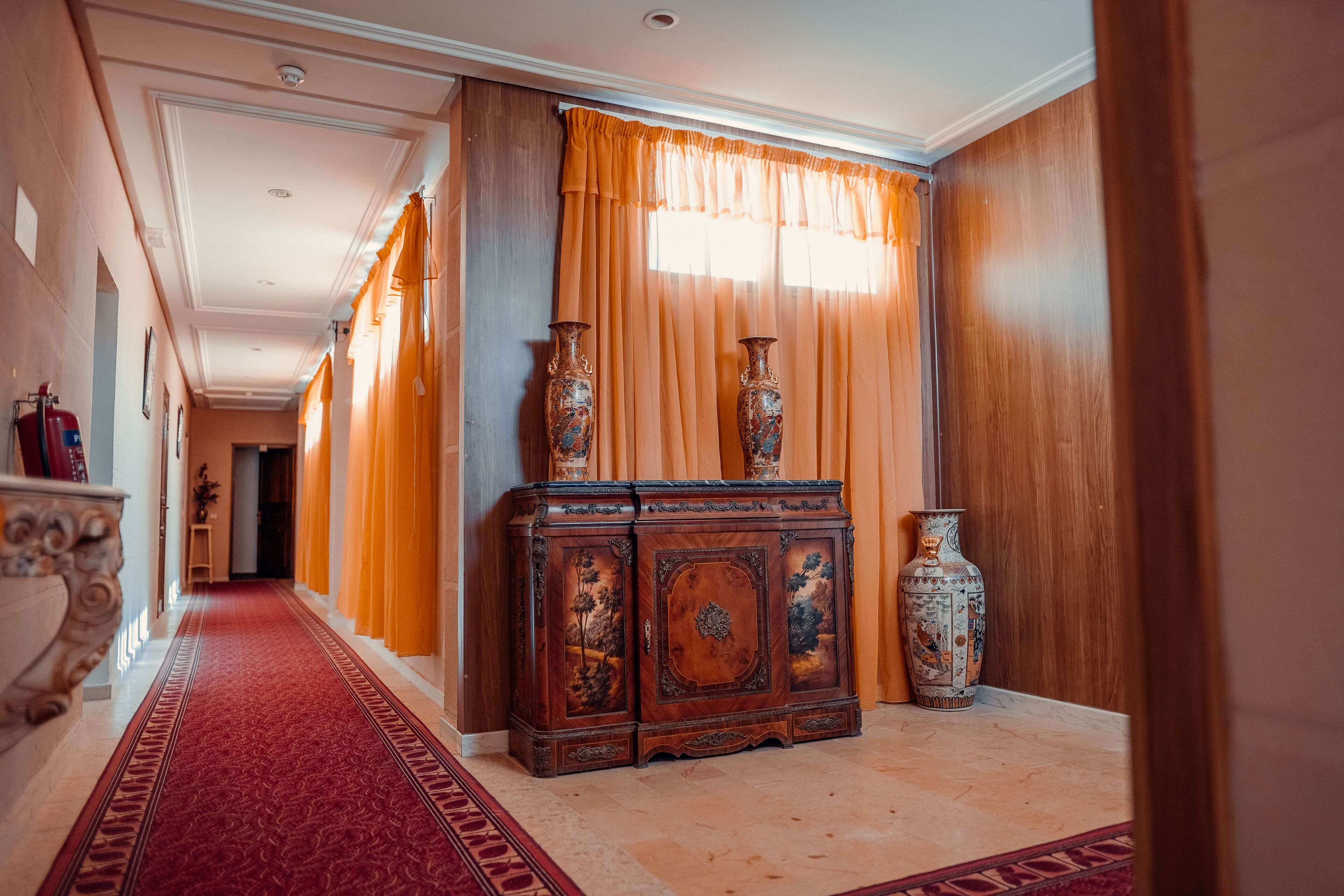 A hallway with a red carpet, wooden paneling, and two large vases on a cabinet.