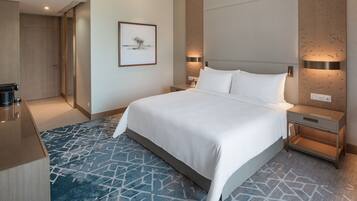 Quarto de hotel moderno com uma cama grande, uma mesa de cabeceira, um criado-mudo, um quadro na parede e um tapete estampado.