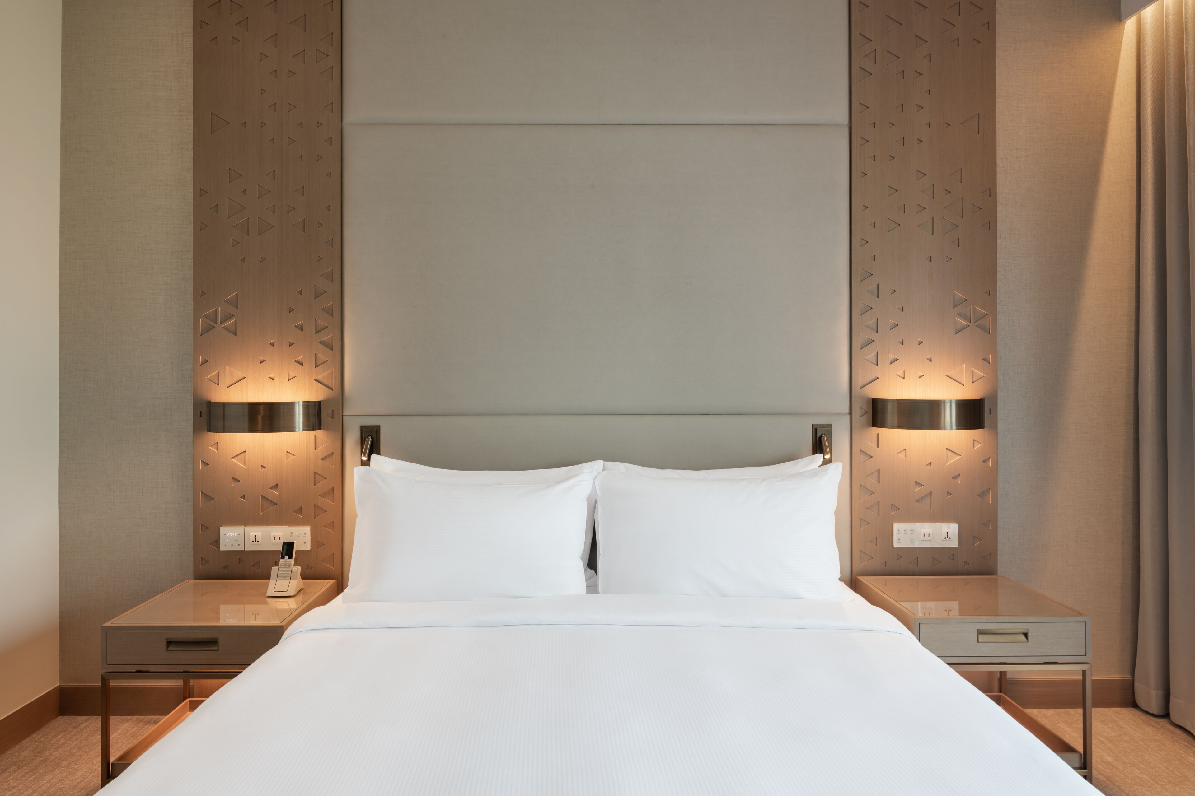 Ein Hotelzimmer mit einem großen Bett, zwei Nachttischen und einem Kopfteil mit geometrischen Mustern.