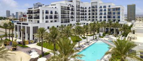 A modern hotel with a rooftop pool, palm trees, and a view of the city skyline.