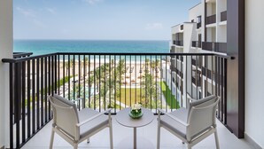 Un balcon avec deux chaises et une table, donnant sur une piscine et une plage.