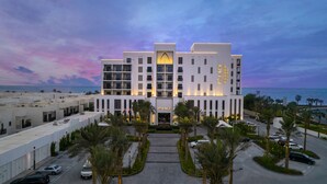 Un hôtel à plusieurs étages, doté d’une entrée imposante, d’un nom évoquant un complexe hôtelier en bord de mer et offrant une vue sur l’océan.