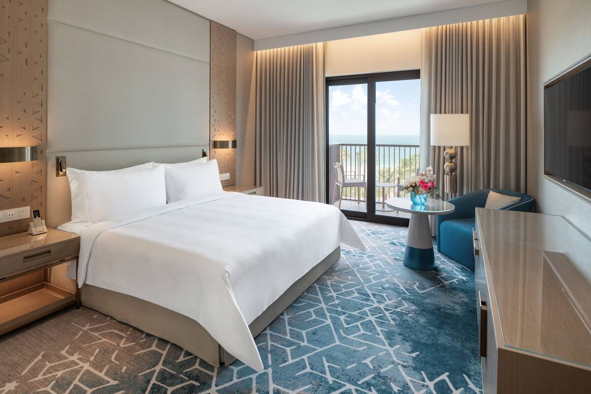 Une chambre d’hôtel avec un grand lit, un bureau, une chaise, une télévision et un balcon avec vue.