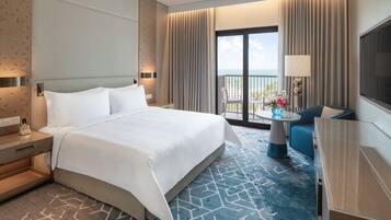 Habitación de hotel con una cama grande, un escritorio, una silla, un televisor y un balcón con vistas.