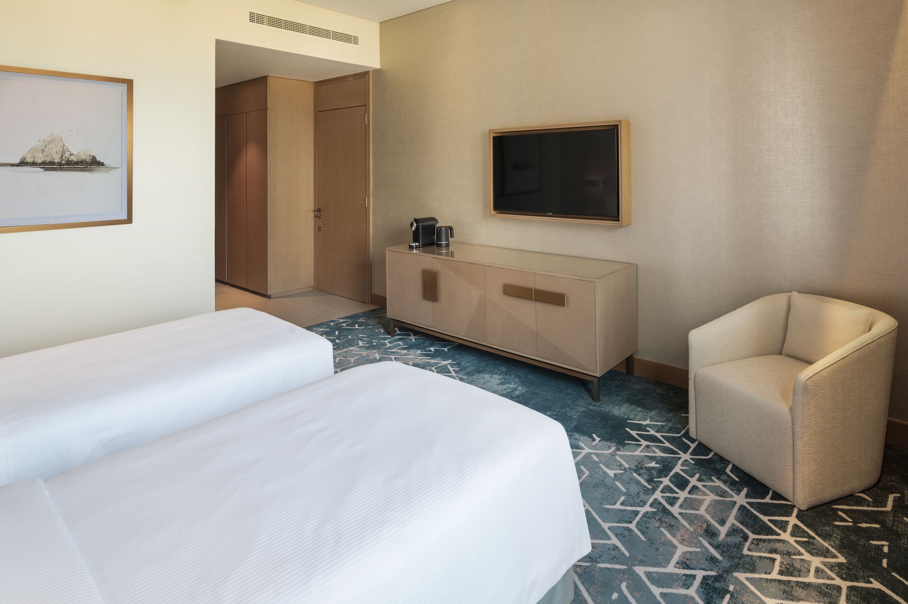 Ein Hotelzimmer mit zwei Betten, einem Fernseher, einer Kaffeemaschine und einem Sessel.