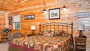Un dormitorio acogedor con techo de madera, una cama con colcha, dos lámparas de noche, una mesita de noche y cuadros enmarcados en la pared.