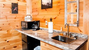 Cocina compacta con paredes de madera, encimera de granito, pileta y electrodomésticos como microondas y refrigerador pequeño.