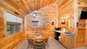 Interior de una cabaña de madera con comedor, cocina y un letrero que dice 'Relax + Sit + Gossip'.