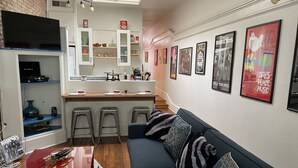 A modern living room with a dark blue sofa, a red coffee table, and a kitchen area with white cabinets and a brick wall. - Lower East Side NYC in Old Bisbee (Bisbee)