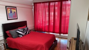 A hotel room with a bed, a television, a window with red curtains, and a framed picture on the wall. - Lower East Side NYC in Old Bisbee (Bisbee)