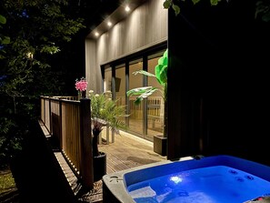 Un edificio moderno con terraza de madera, un jacuzzi y un ventanal grande.