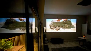 Ett modernt vardagsrum med en stor skärm som visar en filmsnutt, ett träbord och en krukväxt.
