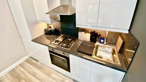 Ett modernt kök med vita skåp, en gasspis, en inbyggd ugn och en diskho i rostfritt stål.