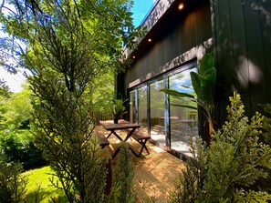 A modern building with large glass windows, a wooden deck, and surrounding lush greenery. - Sunridge Cube 2 with Hot Tub & Giant Home Cinema (Plymouth)