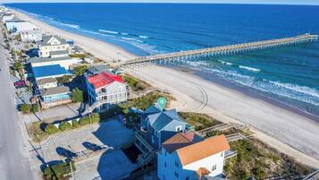 An aerial view of a coastal town with a pier extending into the ocean, beachfront properties, and a clear sky.