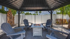 A covered outdoor seating area with a fire feature, surrounded by chairs and a white fence. - Luxurious Modern 4BR, Heated Pool near Beach and Mercato! Newly Renovated! (Naples)