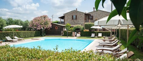 Una piscina con tumbonas, una casa de piedra y un jardín bien cuidado.