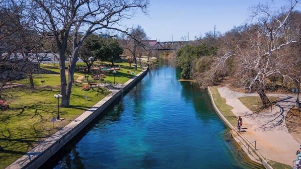 A river with a bridge in the background, surrounded by trees and grassy areas.