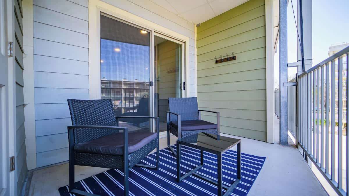 Een balkon met twee stoelen, een kleine tafel, een schuifdeur en een groene wand.