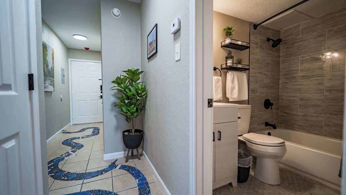 Une salle de bain avec une baignoire, des toilettes et une douche. Il y a une plante dans le coin et le sol est carrelé.