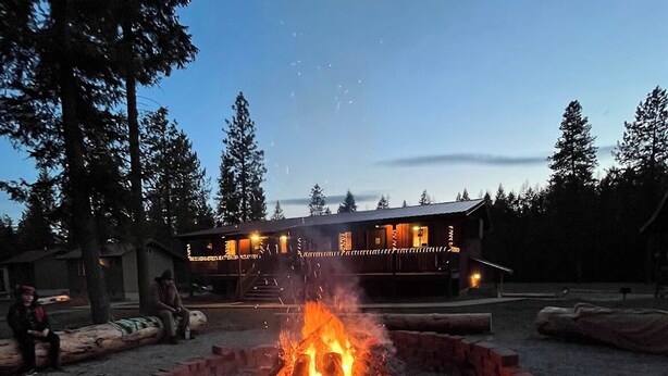 A fire pit in a gravel area with a building in the background. - Bear Creek Resort, Lower Cabin Suite (1 King Bed), Lower Cabin Suite (1 King Bed) (Sanders County)