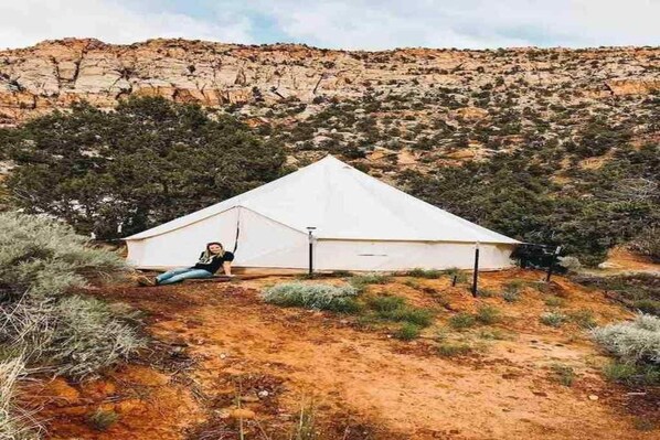 Una tienda blanca en un paisaje desértico con vegetación escasa y colinas rocosas al fondo.