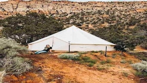 A white tent in a desert landscape with sparse vegetation and rocky hills in the background.