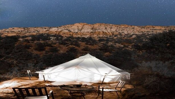 A white tent with a table and chairs set up in a desert landscape at night.