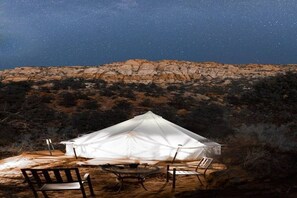 Une tente blanche, avec une table et des chaises installées, se dresse au milieu d’un paysage désertique, de nuit.
