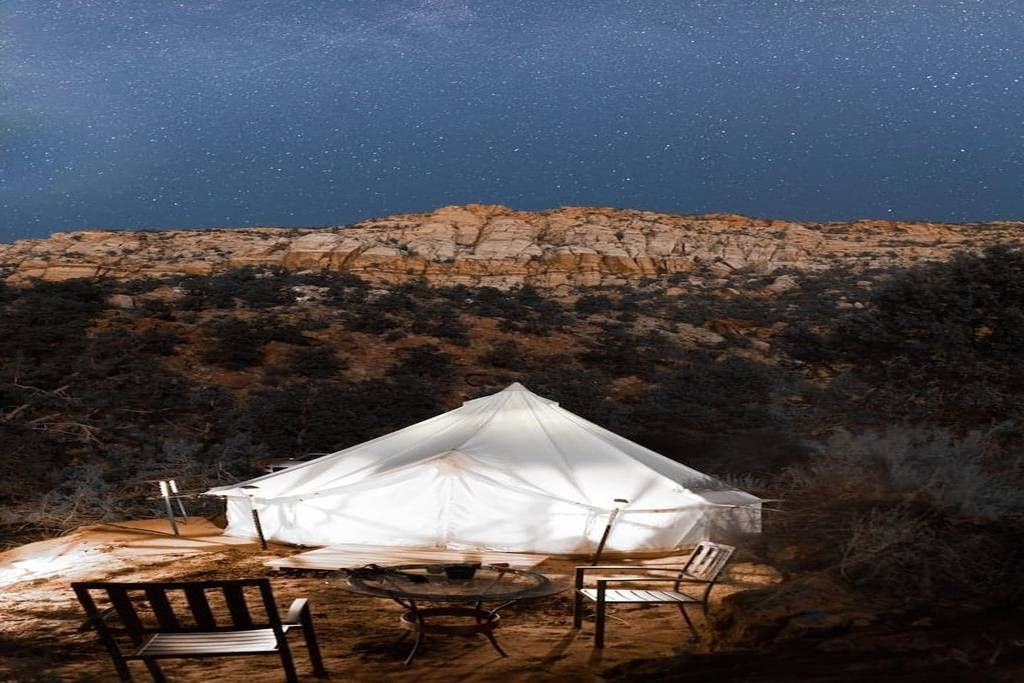 A white tent with a table and chairs set up in a desert landscape at night.