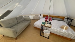 A tent with a bed, a sofa, a small table, and a hanging light.