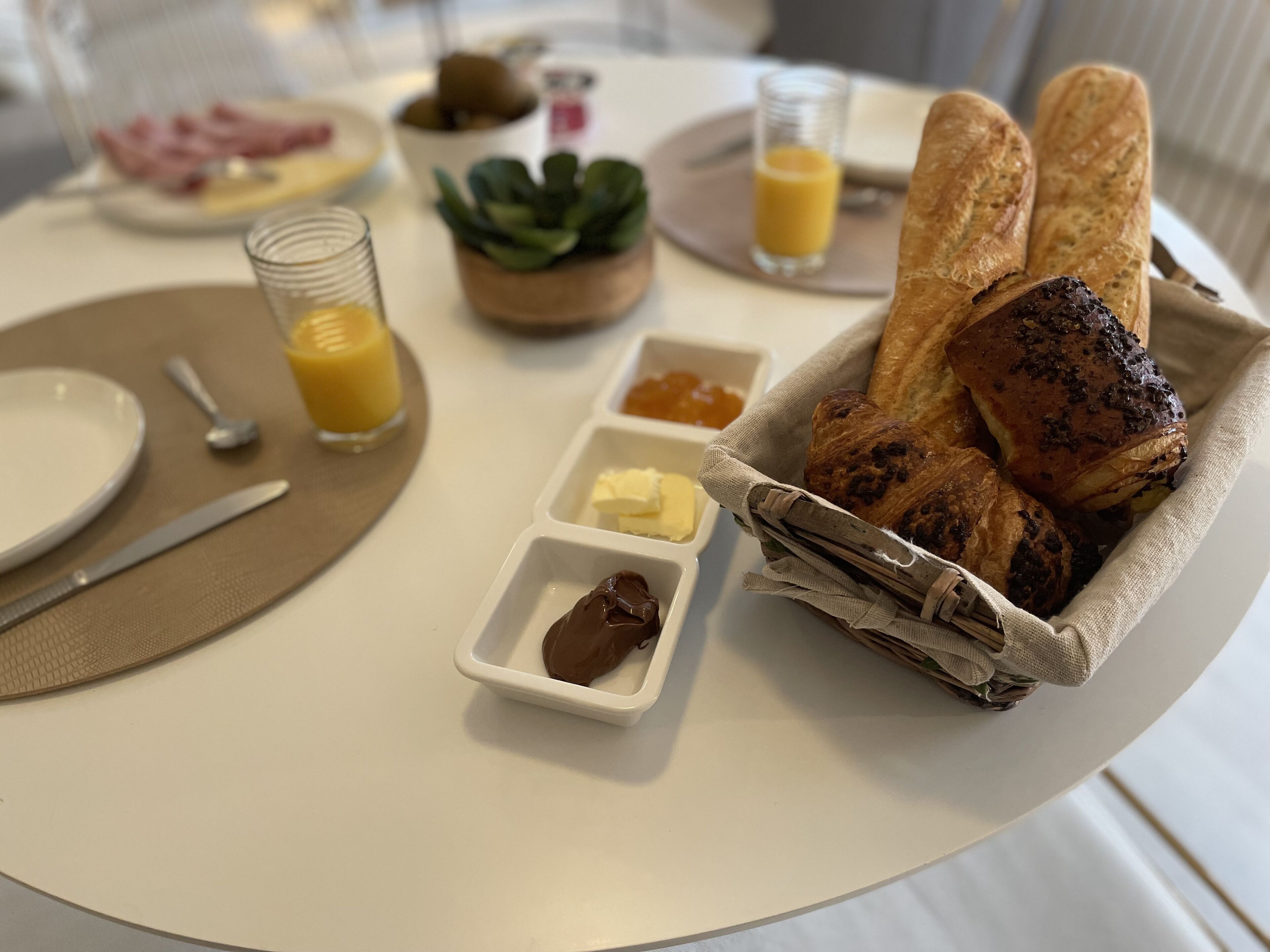 A breakfast setting with bread, butter, jam, and orange juice on a table.