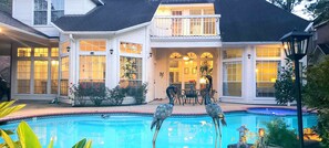 A two-story house with a swimming pool, a balcony, and a patio area with chairs and a table. - Modern Custom Home in Prestigious Champions Golf Club Community (Houston)