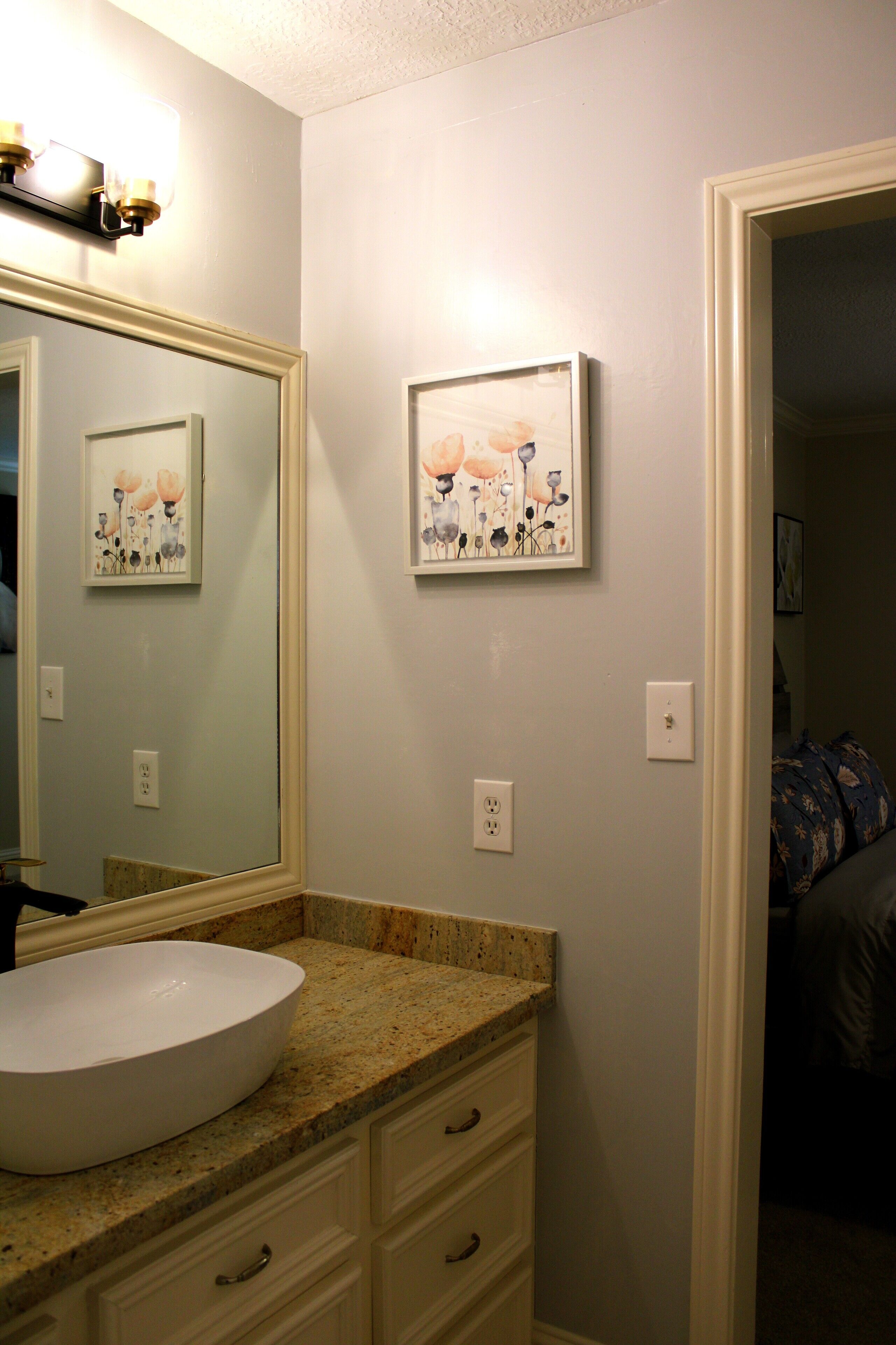 A bathroom with a white sink, a large mirror, and two framed floral paintings on the wall.