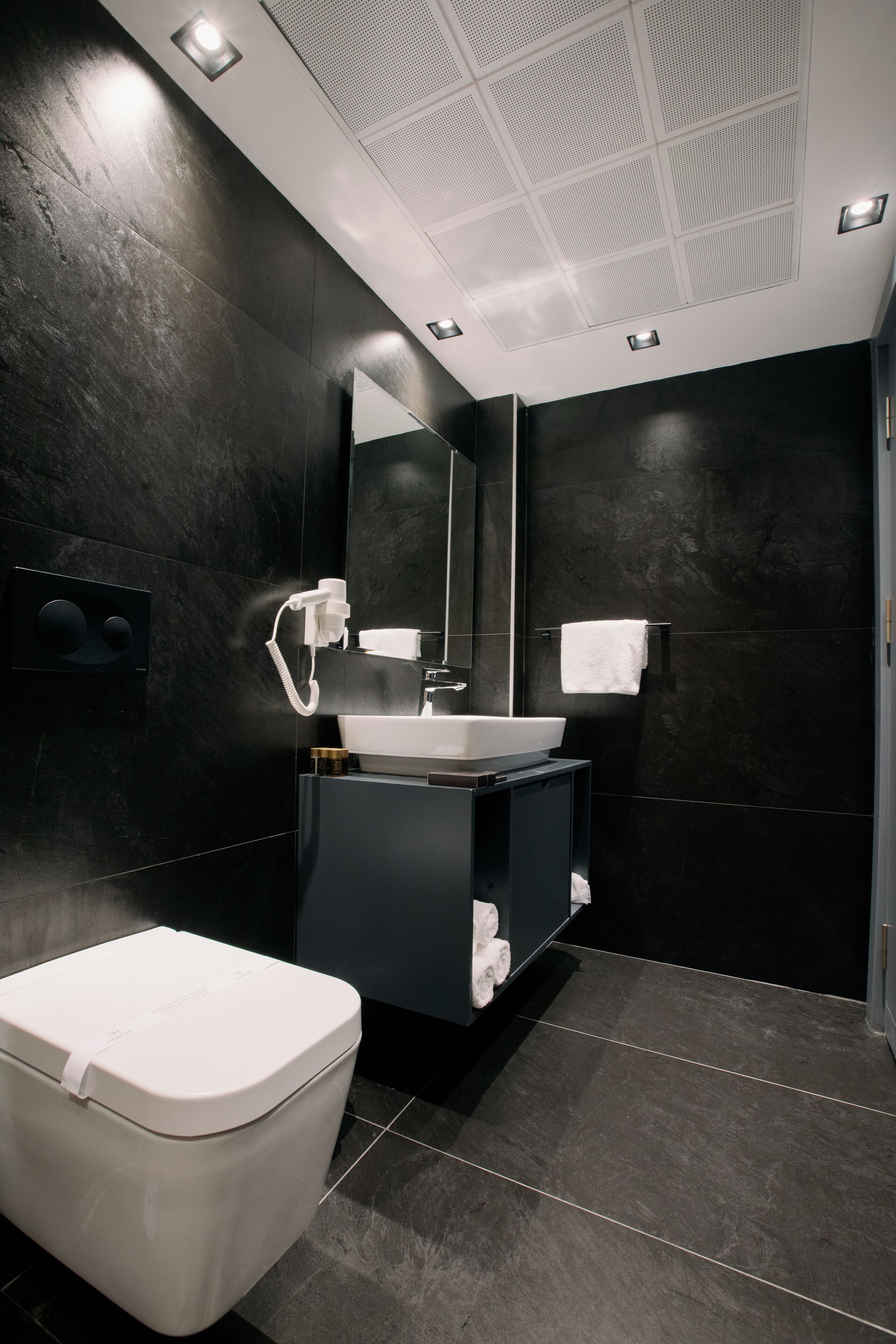 A modern bathroom with a white toilet, a black sink vanity, and a large mirror.
